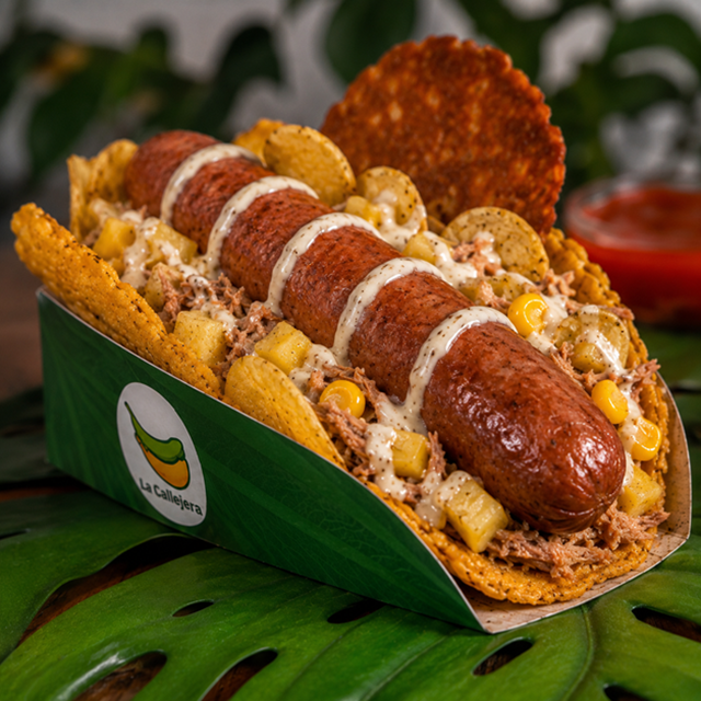 La Callejera: tostón pintón con salchicha, cerdo, salsa de ajo, papa chips, piña y maíz tierno